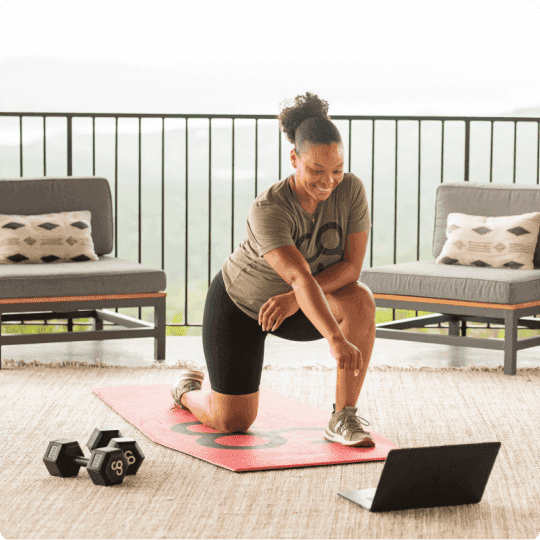 Woman with workout clothes at a balcony kneeling with her fist closed point towards a laptop on the floor